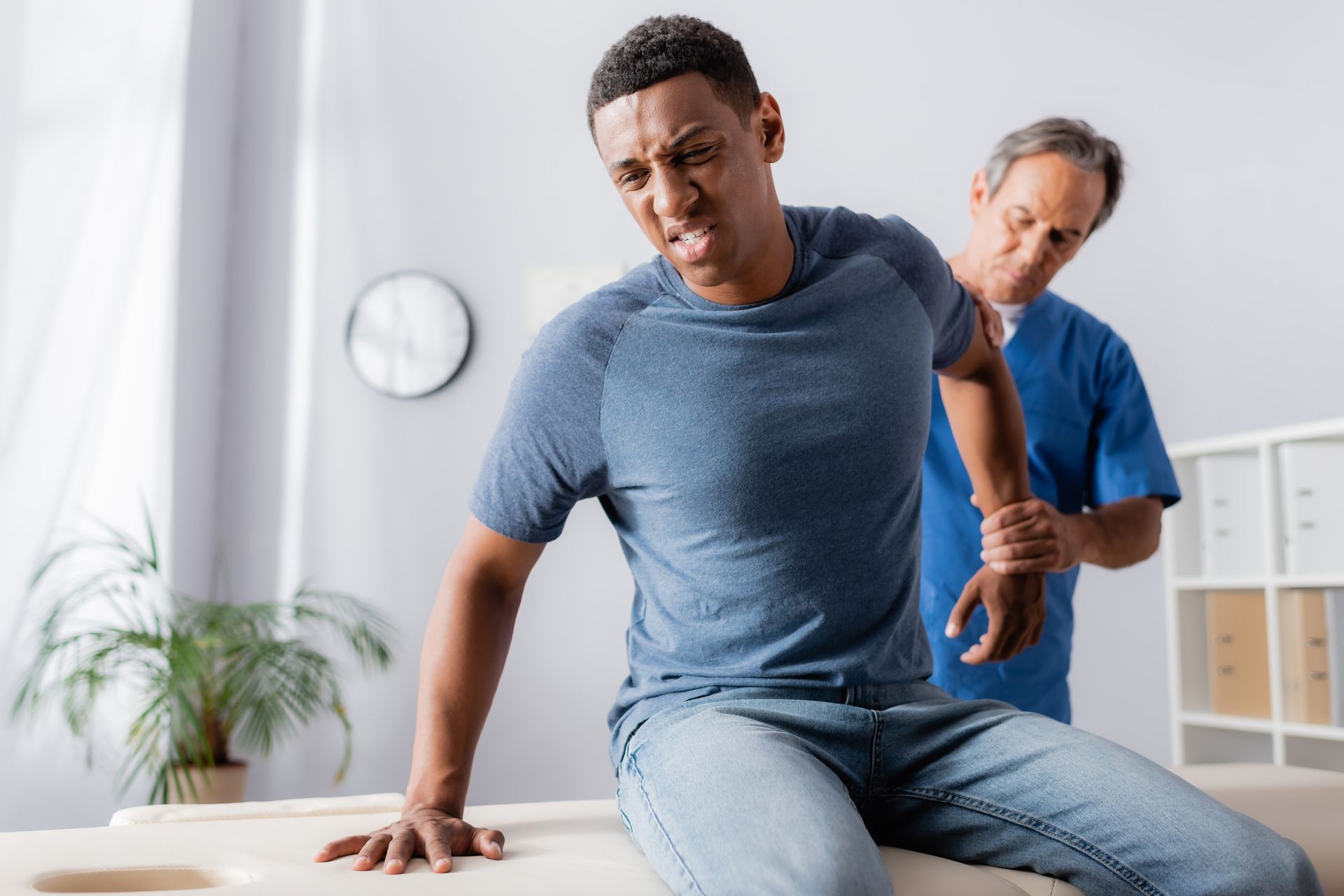 Man in discomfort getting physical therapy on arm by a medical professional in a clinic setting.